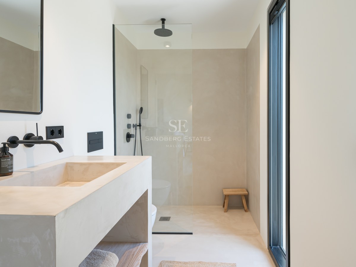 Salle de bain moderne avec lavabo en microciment, robinetterie noir mat et douche à l'italienne vitrée.