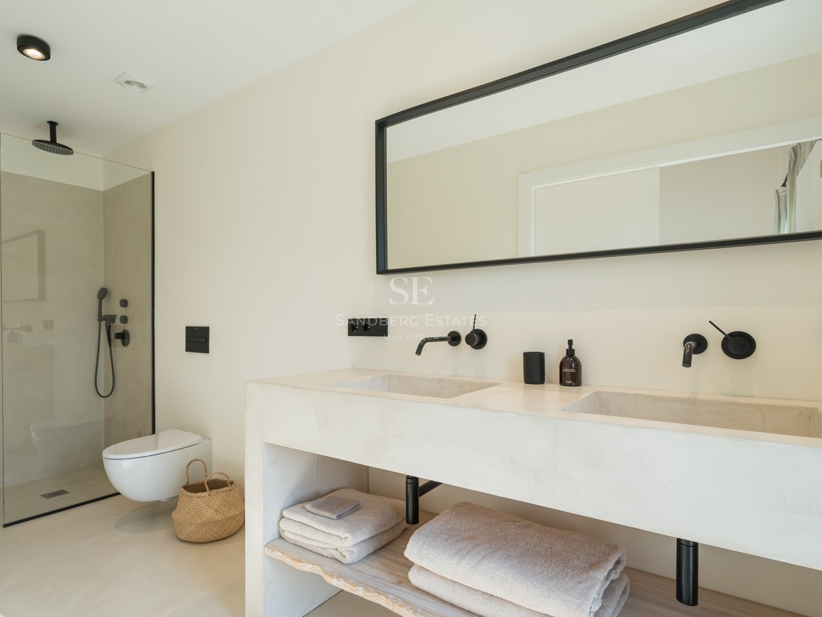 Salle de bains minimaliste avec double vasque, robinetterie noire mate, douche à l'italienne et finitions microciment.