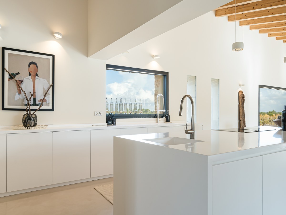 Cuisine blanche minimaliste avec îlot, plans de travail en quartz et plafond en poutres de bois naturel.