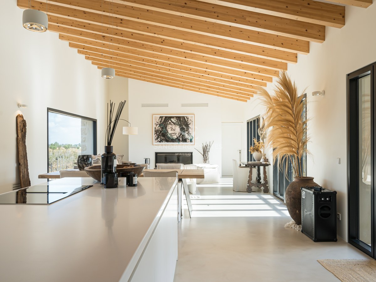 Cuisine moderne avec îlot blanc, hauts plafonds en bois et grandes baies vitrées donnant sur l'extérieur.