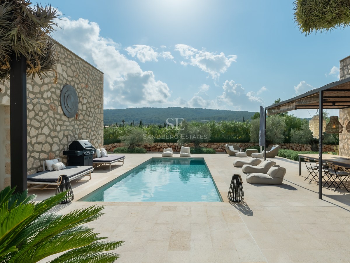 Piscine rectangulaire turquoise entourée d'une terrasse en pierre, coin repas extérieur et murs en pierre naturelle.