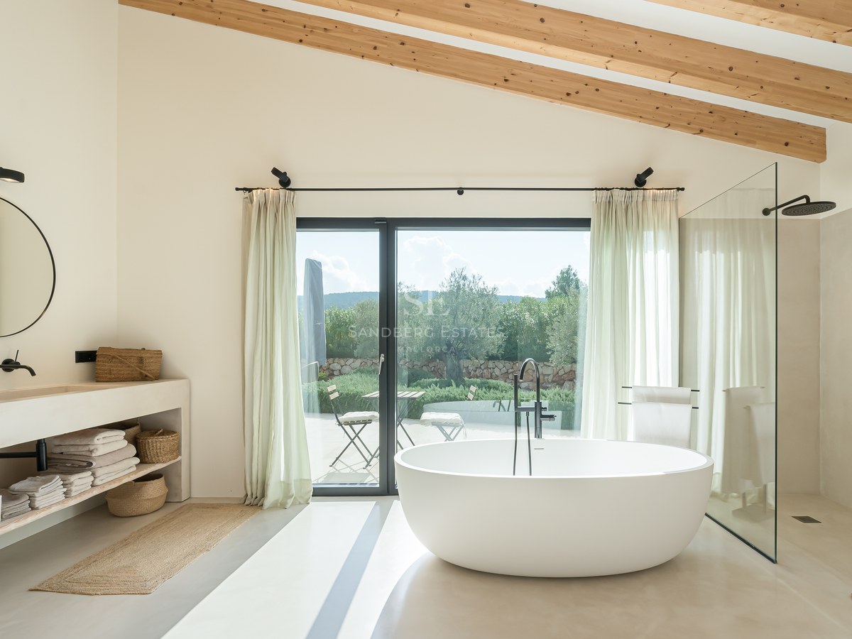 Salle de bain moderne avec baignoire îlot, poutres en bois, douche à l'italienne et accès terrasse paysagée.