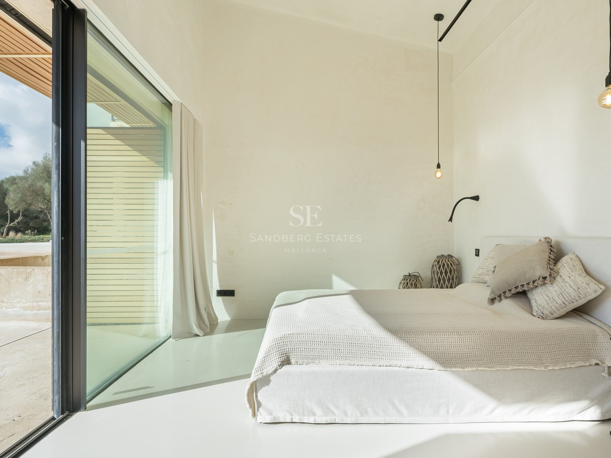 Chambre minimaliste lumineuse avec murs blancs, grande baie vitrée et literie aux tons neutres.
