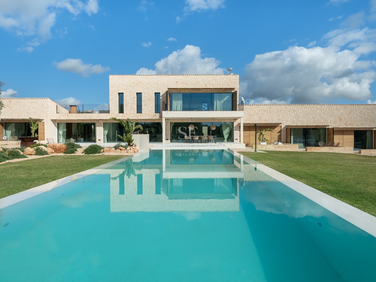 Villa moderne de deux étages avec une grande piscine rectangulaire et une façade en pierre naturelle sous un ciel bleu.