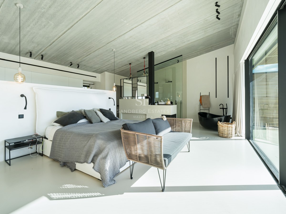 Chambre de maître moderne à aire ouverte avec plafond en béton, lit gris et baignoire îlot noire.