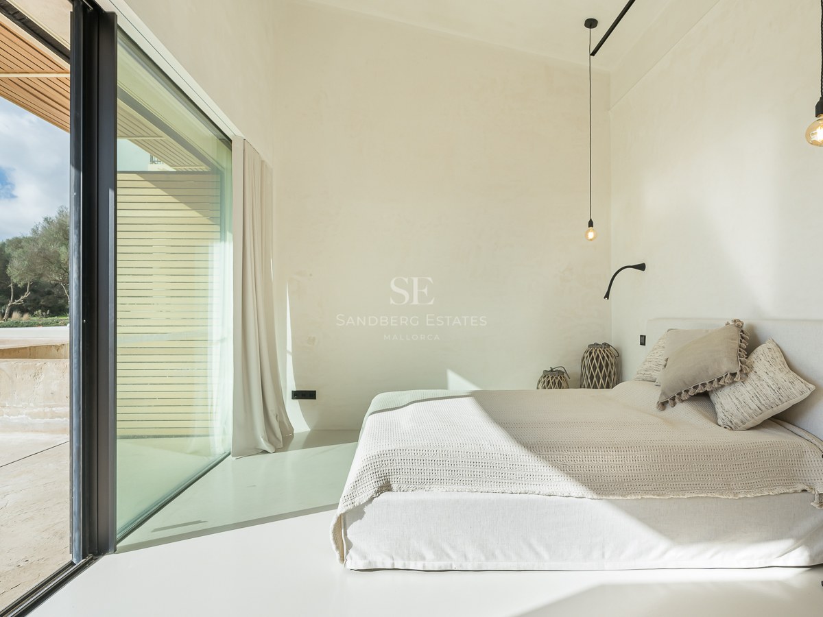 Chambre lumineuse au design minimaliste avec lit blanc, grandes baies vitrées et balcon privé.