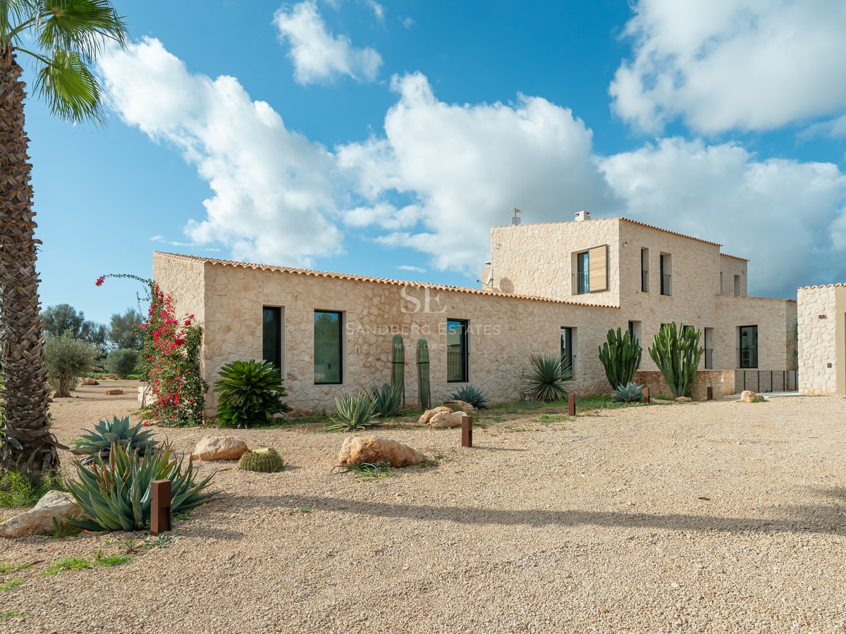 Façade en pierre naturelle d'une villa moderne avec jardin de cactus et allée en gravier sous un ciel bleu.