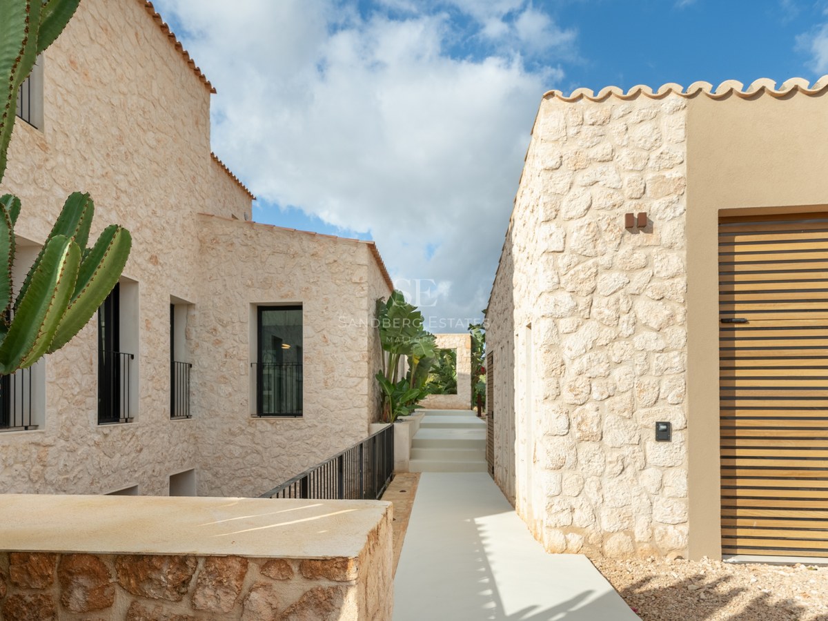 Allée minimaliste en pierre naturelle entre deux bâtiments de villas contemporaines sous un ciel bleu.
