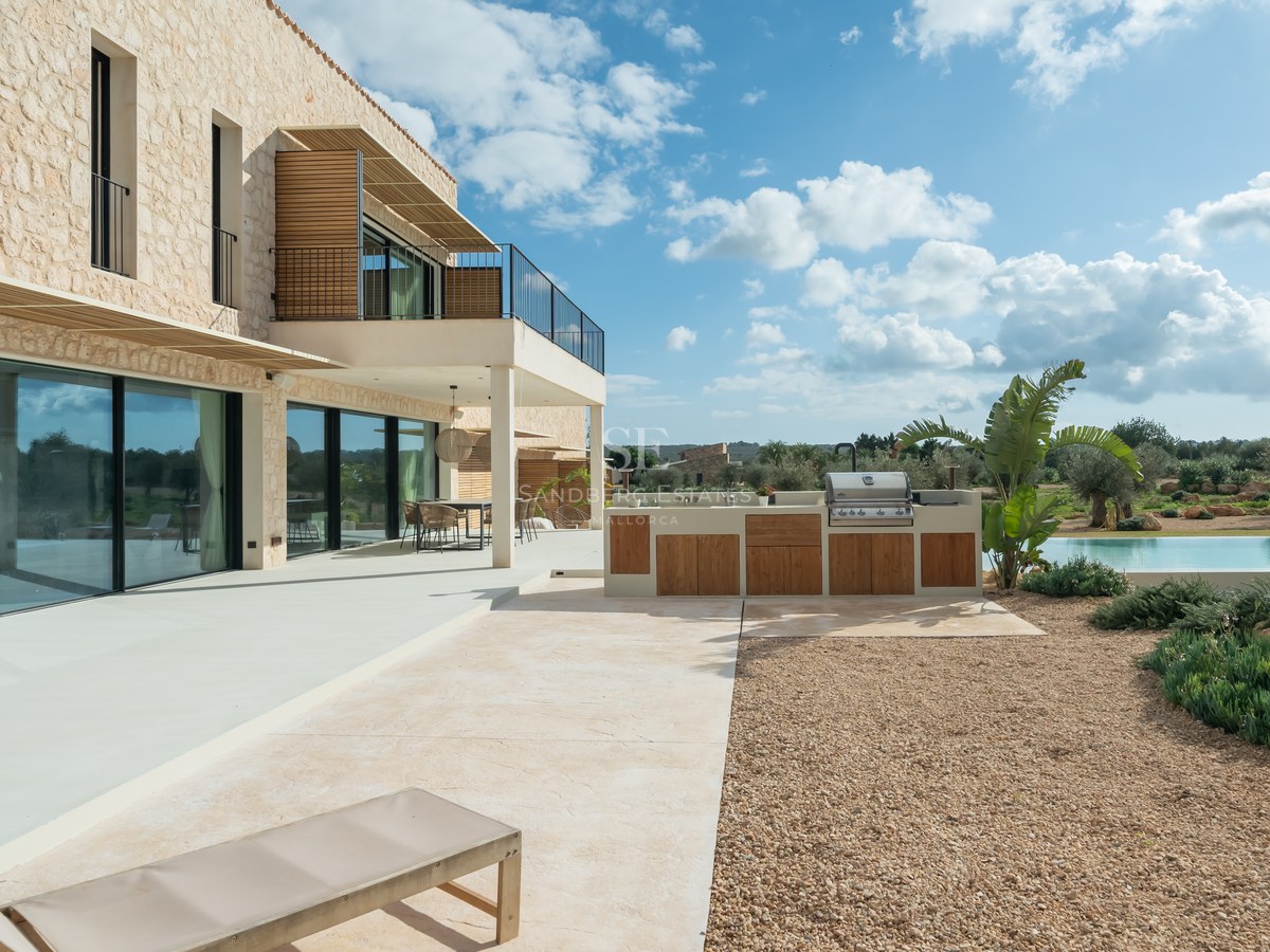 Terrasse moderne avec cuisine d'été en bois, façade en pierre naturelle et larges baies vitrées.