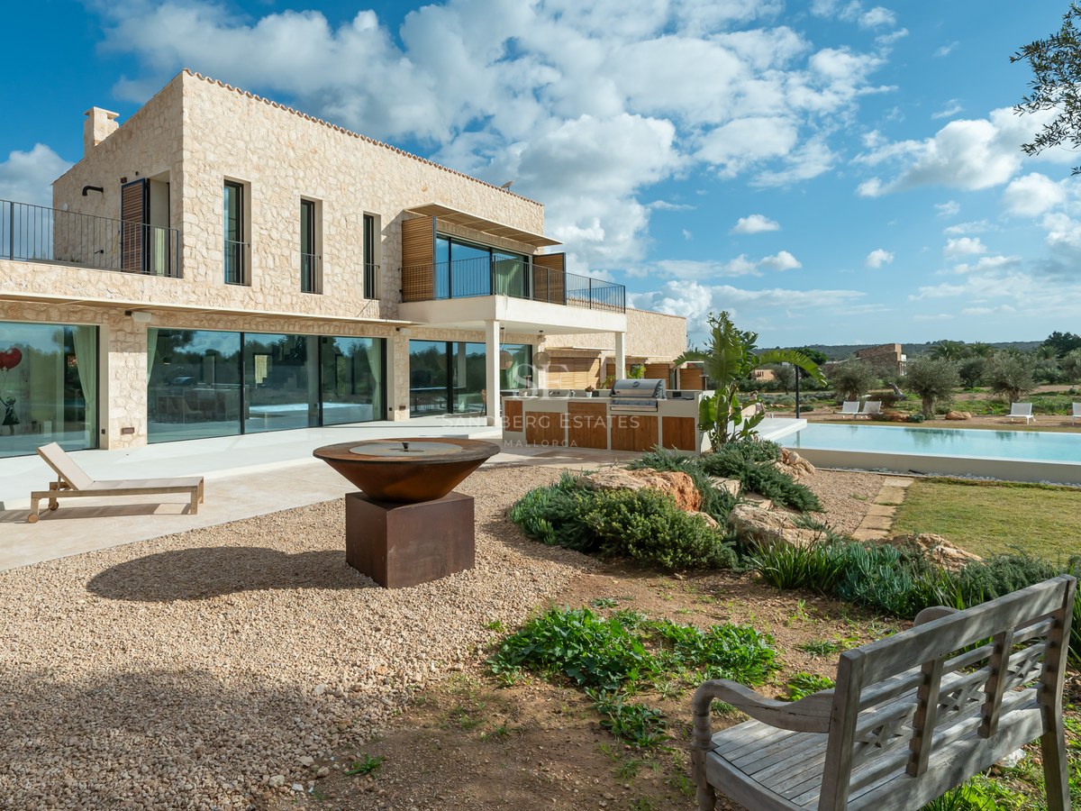 Villa moderne à deux étages avec murs en pierre naturelle, grandes baies vitrées, cuisine d'été et brasero extérieur.