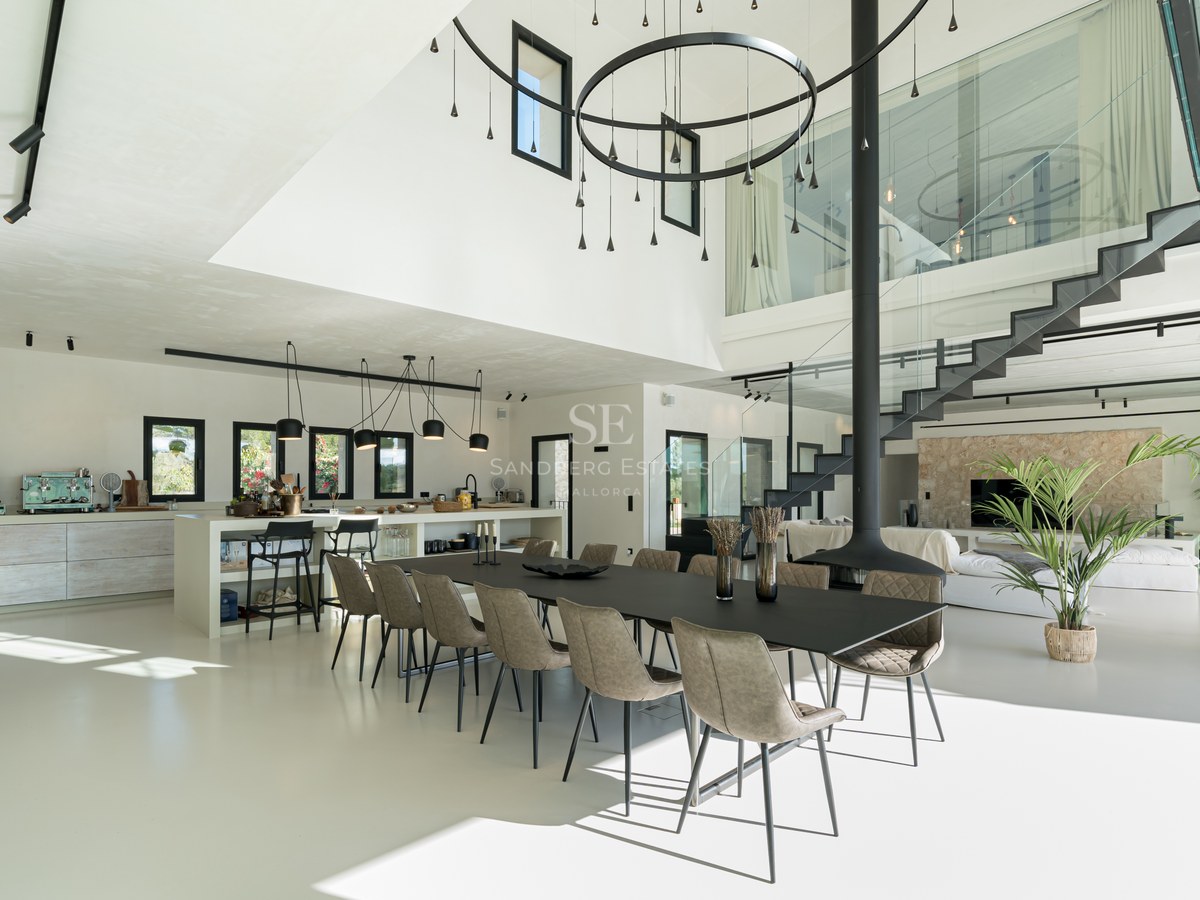 Salle à manger moderne avec grande table noire, cheminée suspendue et mezzanine vitrée sous plafond haut.
