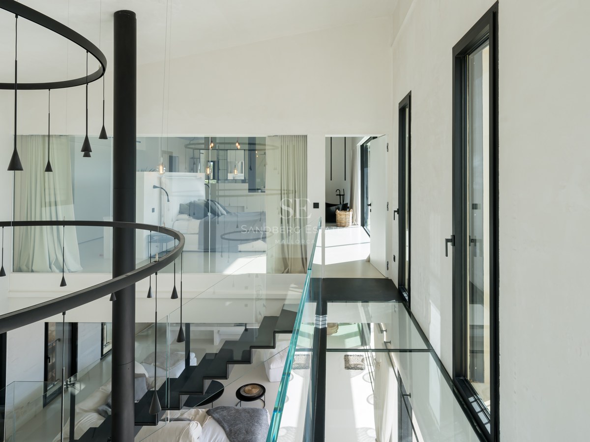 Couloir intérieur moderne avec passerelle en verre, escalier noir et grandes fenêtres dans une villa contemporaine.