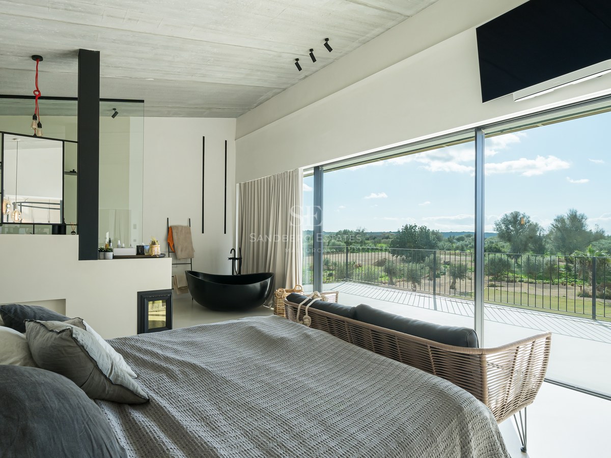 Chambre de maître moderne avec baignoire noire, cheminée et baies vitrées donnant sur la campagne.