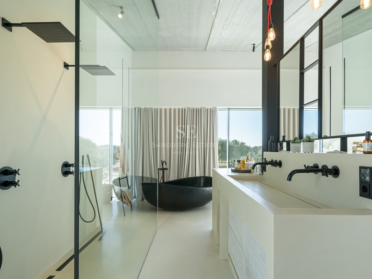 Salle de bains minimaliste avec baignoire îlot noire, double vasque blanche et grandes baies vitrées.