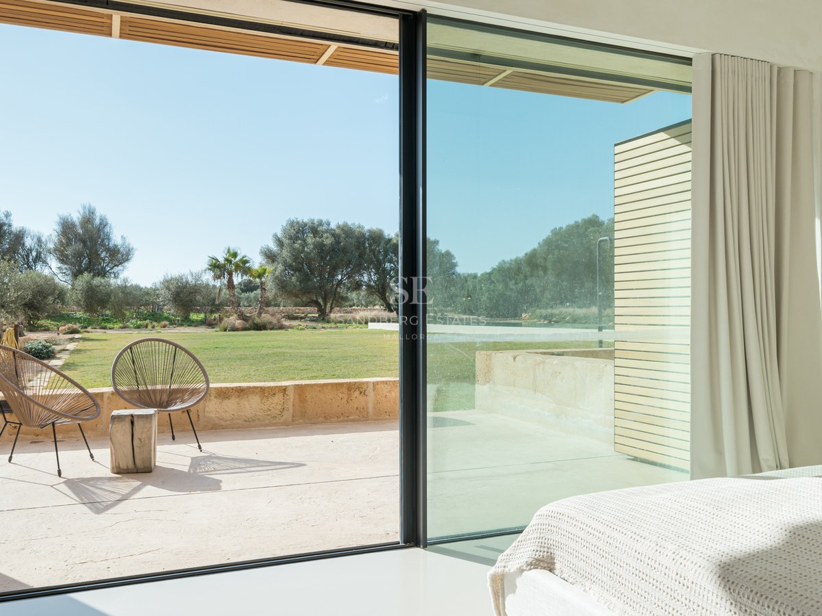 Vue depuis une chambre à travers des baies vitrées coulissantes sur une terrasse ensoleillée et un jardin paysager.