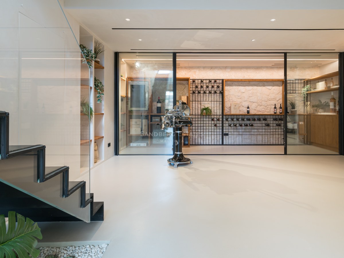 Cave à vin moderne vitrée avec mur en pierre, étagères sur mesure et escalier minimaliste dans une villa de luxe.