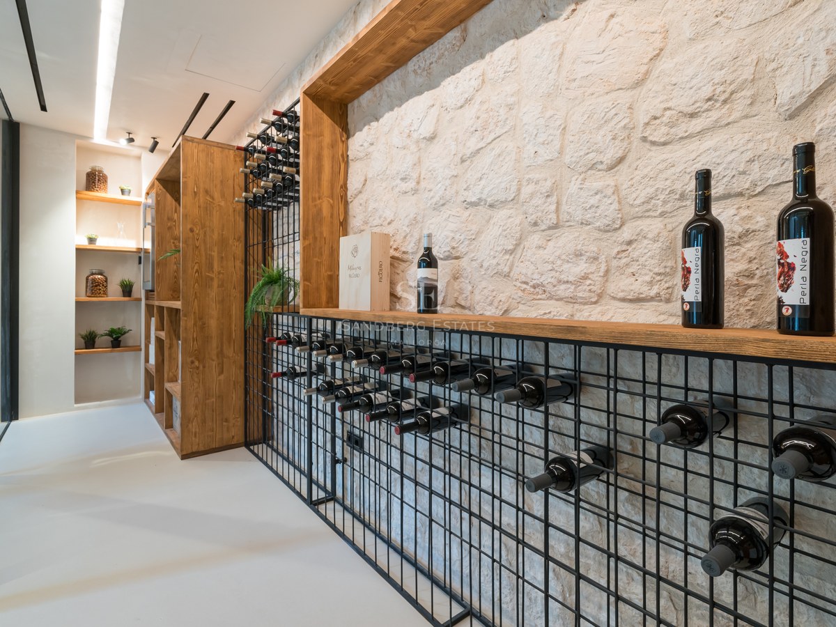 Cave à vin moderne avec mur en pierre blanche, casiers en métal noir et finitions en bois clair.