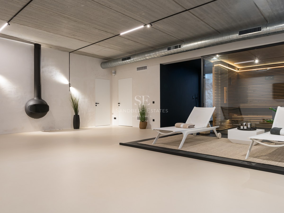 Spa intérieur minimaliste avec sauna en bois et verre, chaise longue blanche et finitions industrielles.