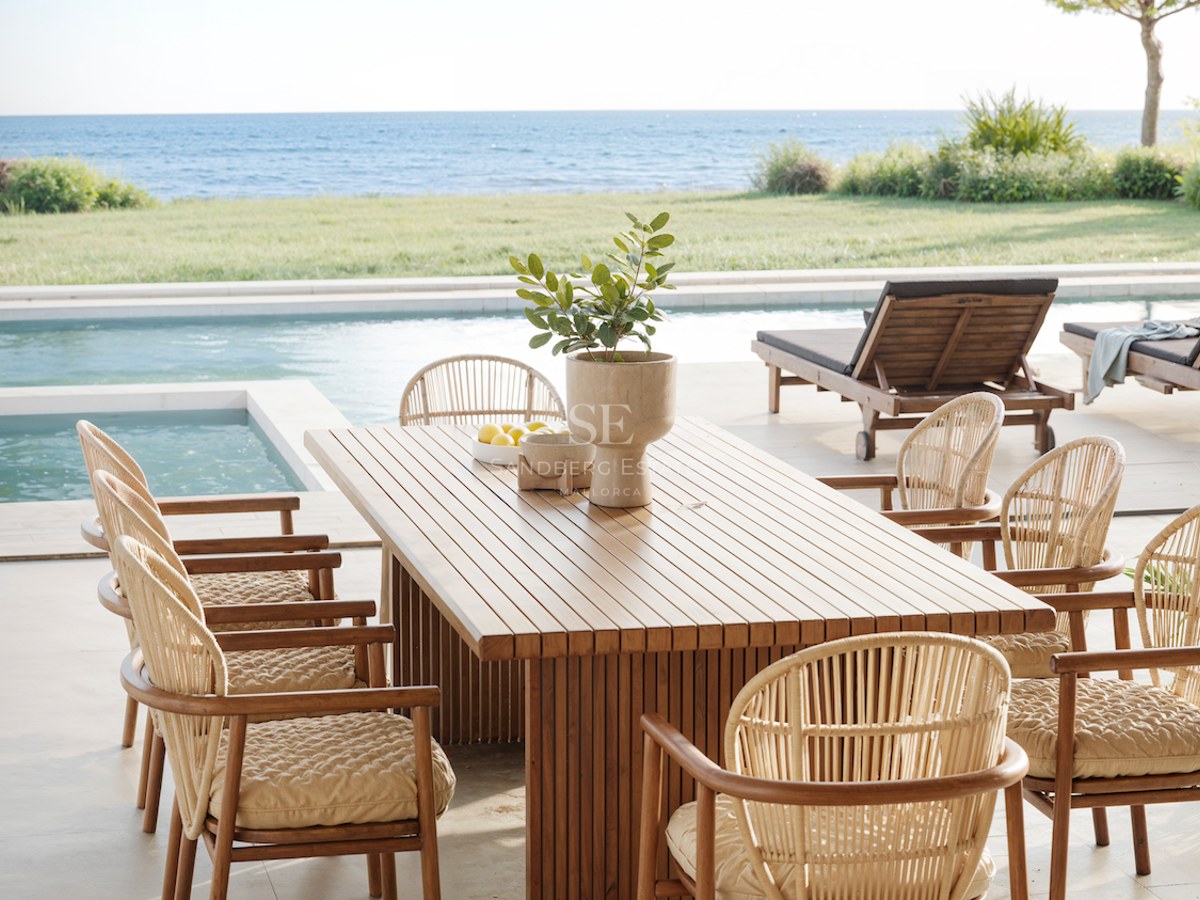 Table à manger en bois et chaises en osier sur une terrasse surplombant une piscine et la mer Méditerranée.
