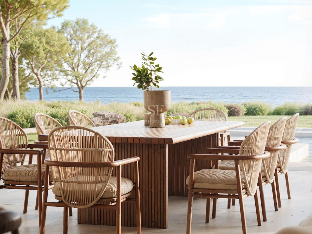 Une table à manger en bois et six chaises en osier sur une terrasse en pierre surplombant la mer Méditerranée.