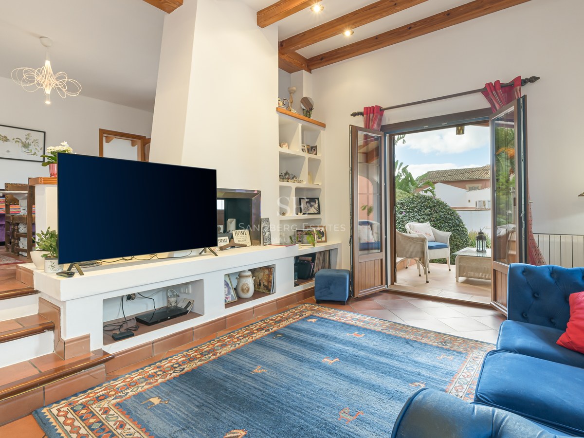 Living room featuring terracotta floors, exposed wooden beams, and open French doors leading to a sunlit terrace.