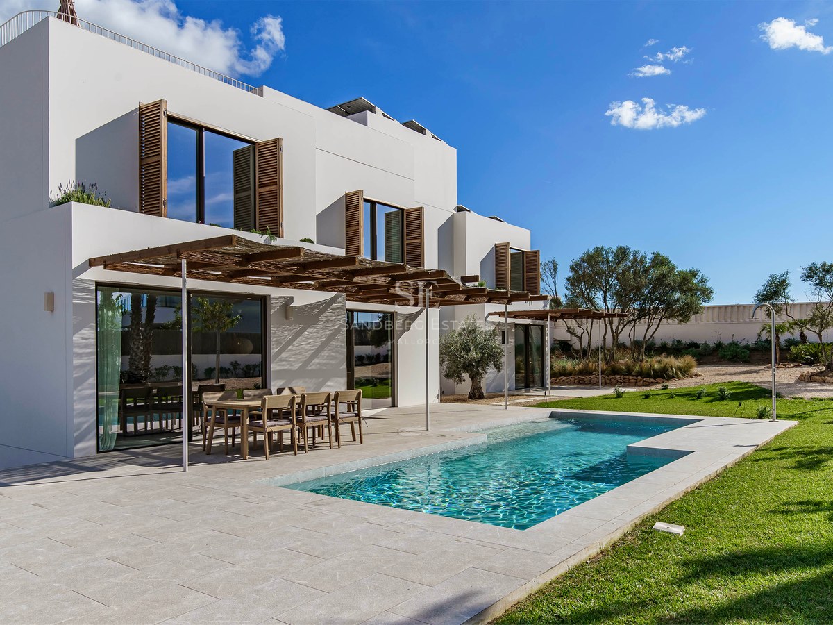 Exteriör av en vit modern villa med pool, träpergola och gräsmatta under en blå himmel.