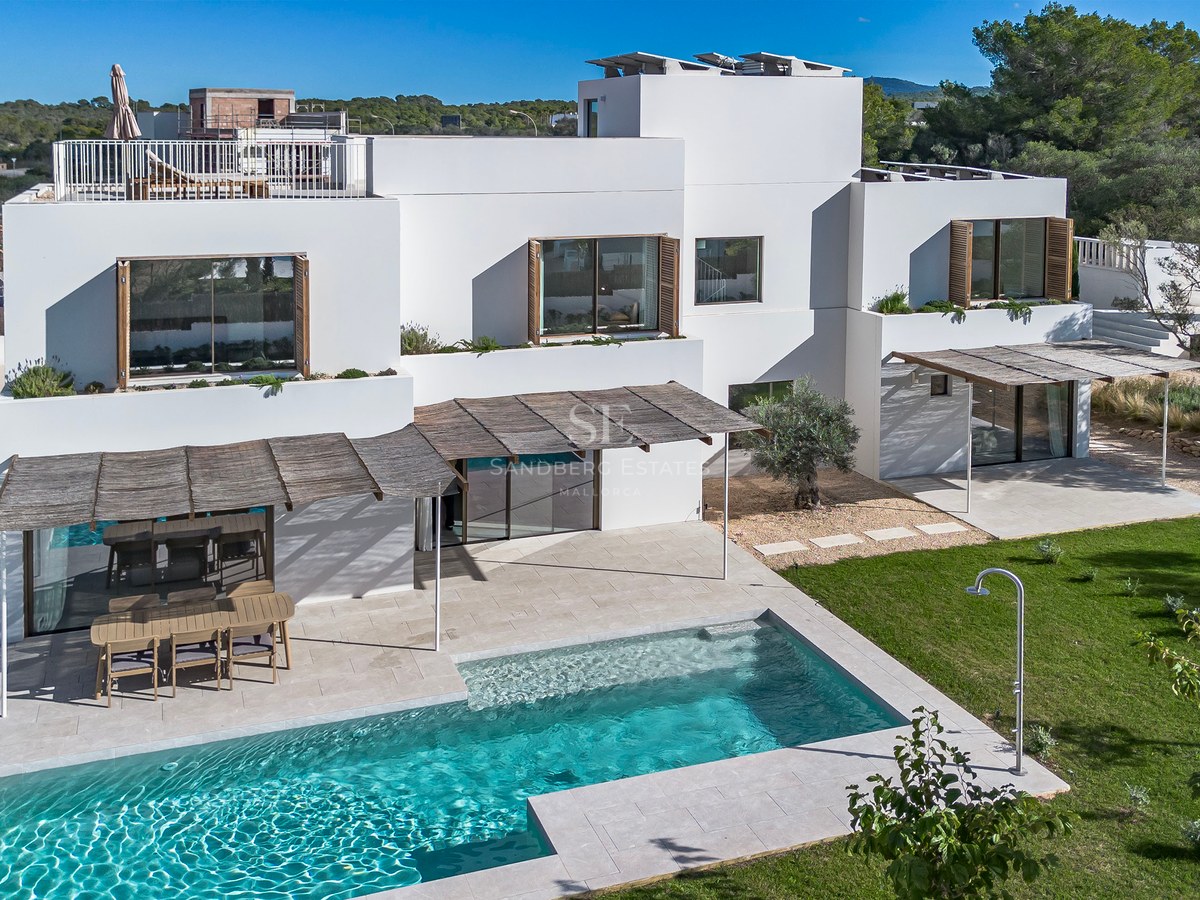 Flygvy över en vit samtida villa med turkos pool, stenterrass och grönskande trädgård.