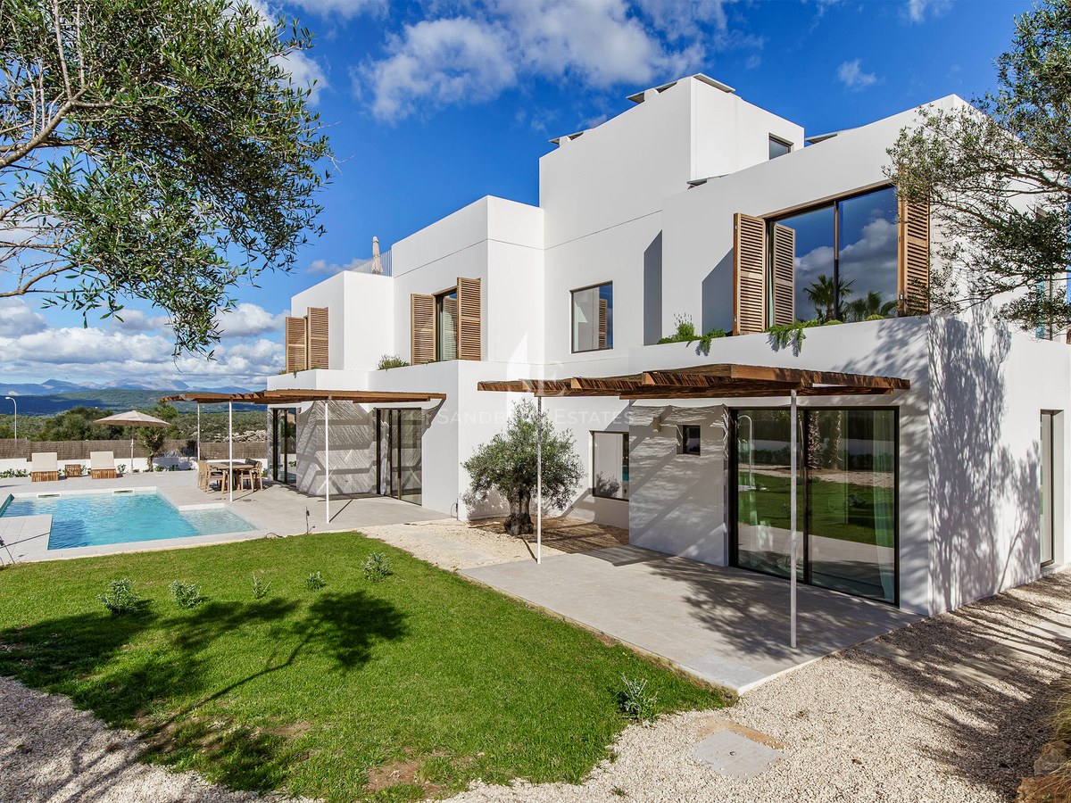 Modern vit villa med turkos pool, träpergola och olivträd under en blå himmel.