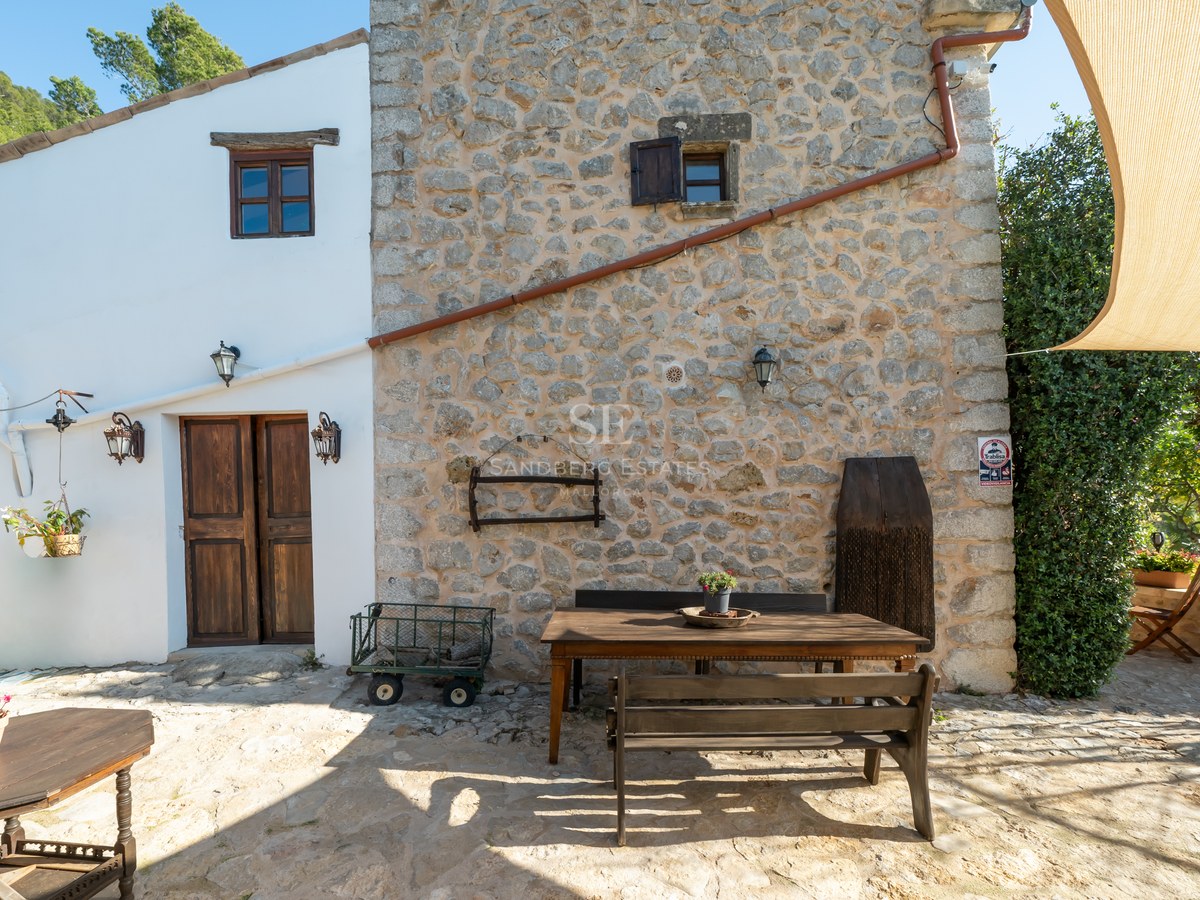 Mur en pierre authentique, porte en bois, volets et table à manger extérieure sur une terrasse ensoleillée.