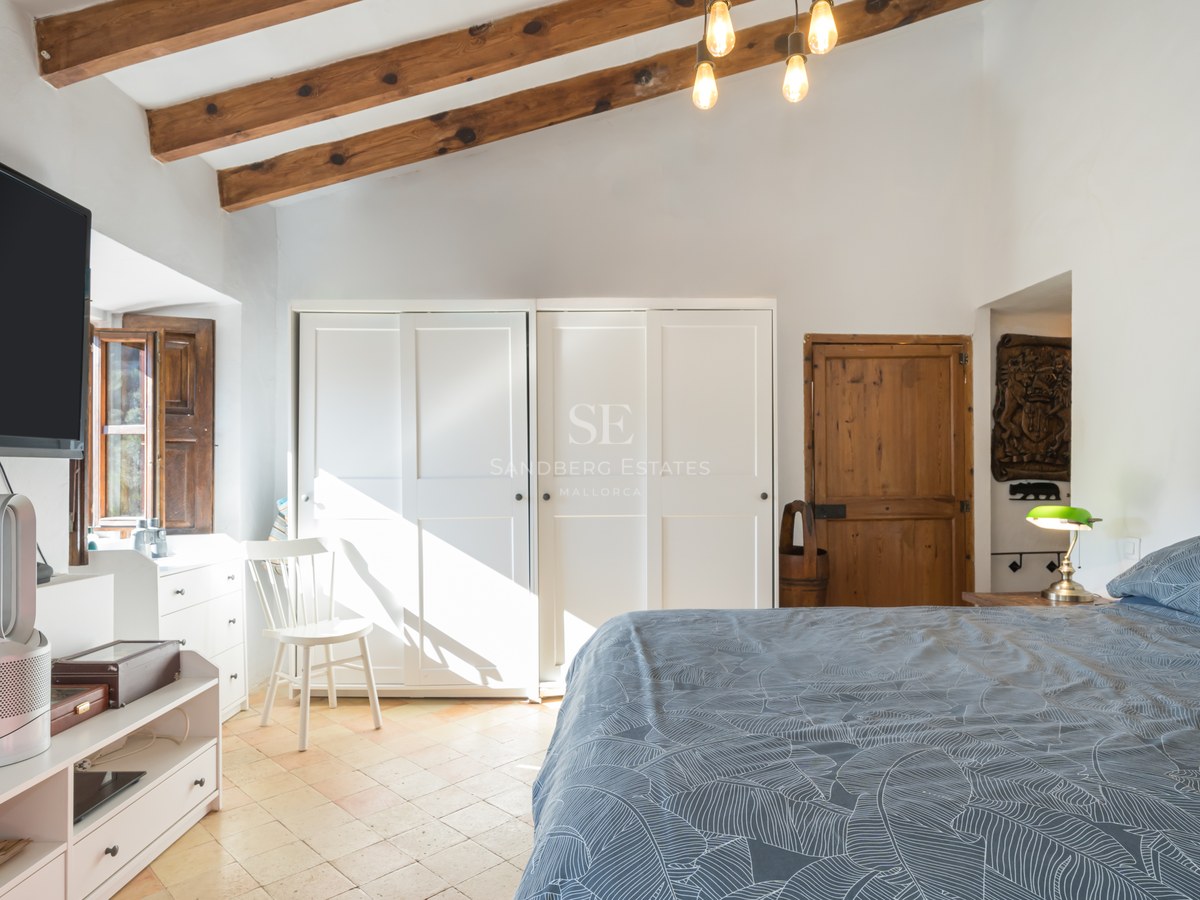 Chambre lumineuse avec poutres de plafond en bois, armoires encastrées blanches et parquet clair.