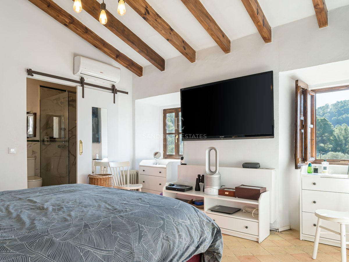 Chambre disposant de poutres en bois au plafond, d'un téléviseur mural et d'une porte coulissante blanche.