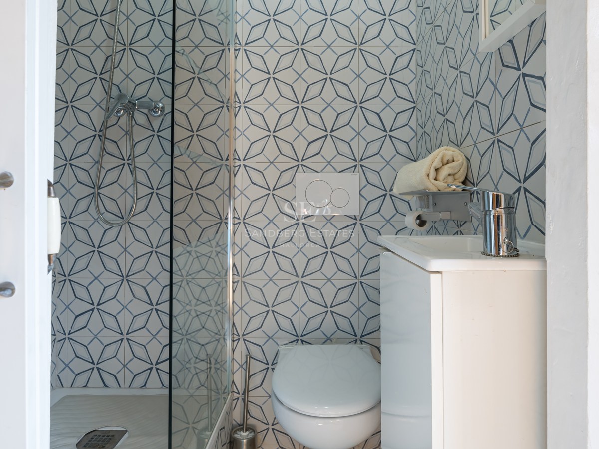 Salle de bains contemporaine avec carreaux géométriques bleus et blancs, paroi de douche en verre et vasque blanche.