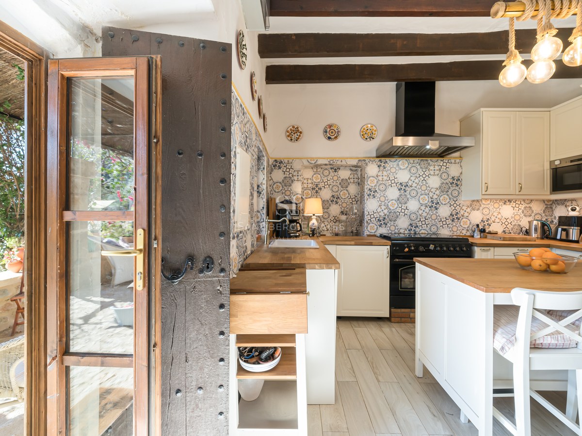 Cuisine rustique avec crédence en carreaux de ciment, poutres en bois sombre et porte traditionnelle cloutée.