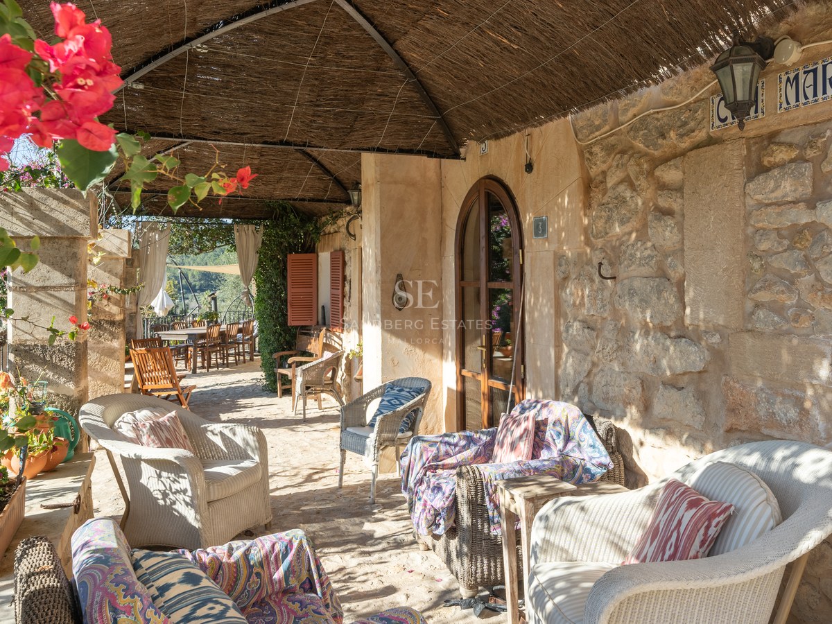 Une terrasse couverte avec des murs en pierre, des fauteuils en osier et un toit traditionnel en canisse.