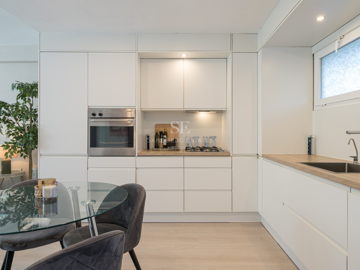 White minimalist kitchen with integrated Miele oven, wood-effect countertops, and a glass dining table with velvet chairs.
