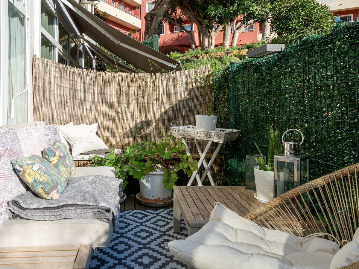 Sunny terrace featuring comfortable sofas, a geometric rug, and bamboo privacy screening in a coastal setting.