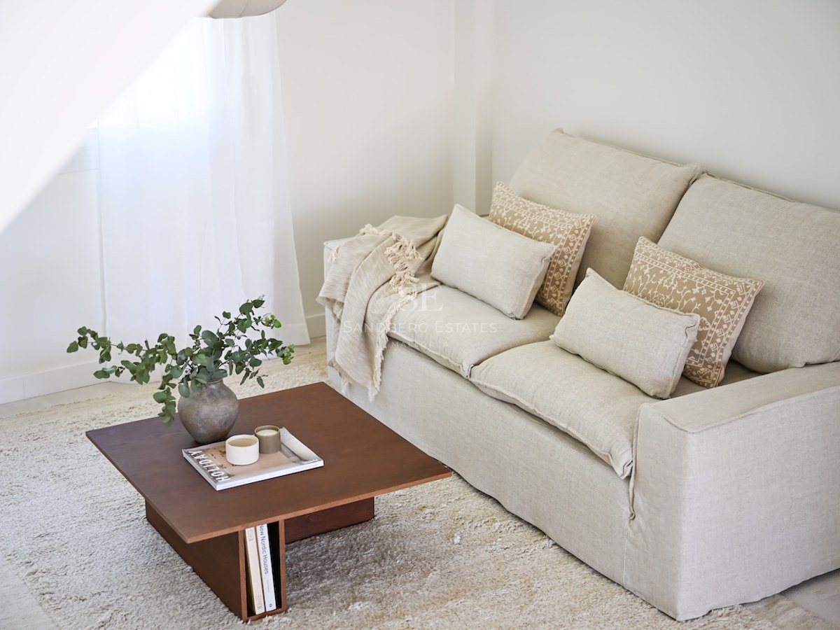 Salón minimalista con sofá de lino beige, mesa de centro de madera con eucalipto y alfombra de color crema texturizada.