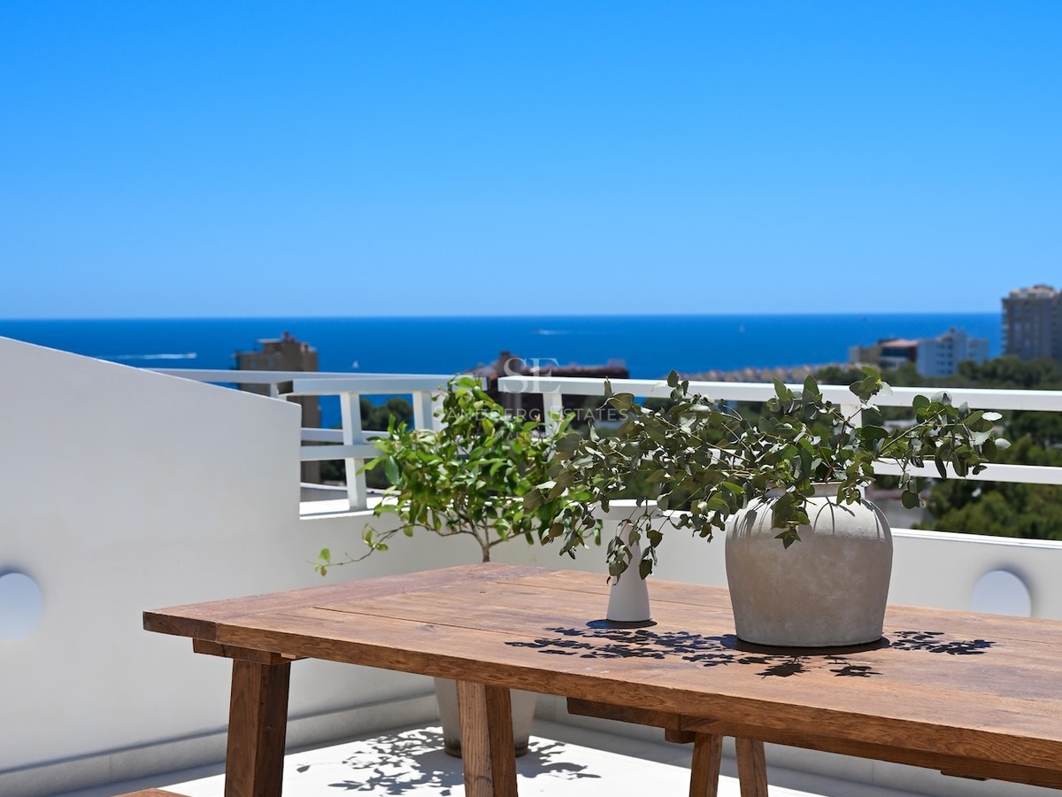 Mesa de madera rústica en una terraza blanca con vistas al mar azul profundo bajo un cielo despejado.