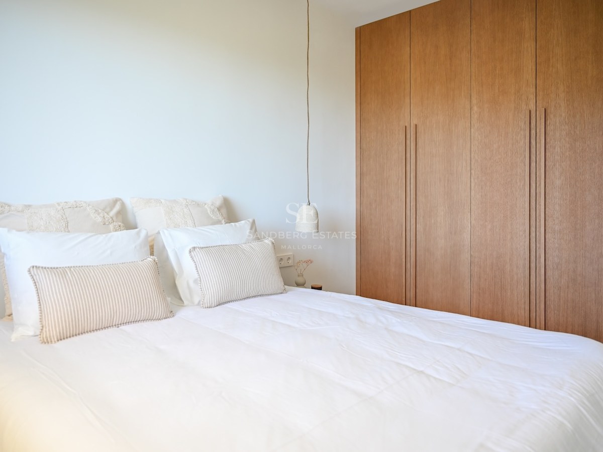 Dormitorio luminoso con cama blanca, cojines a rayas y grandes armarios empotrados de madera de suelo a techo.