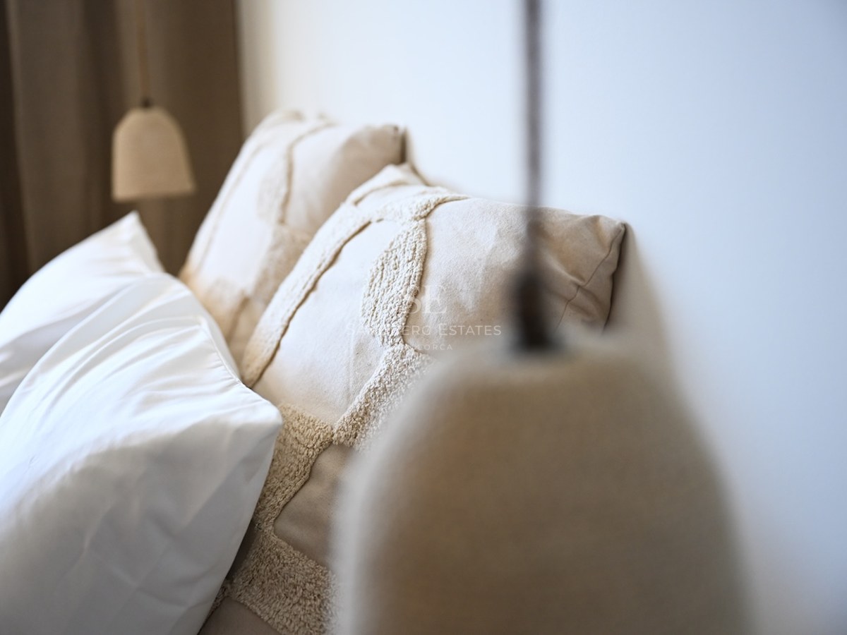Närbild på texturerade linnekuddar och en minimalistisk taklampa i ett ljust sovrum.