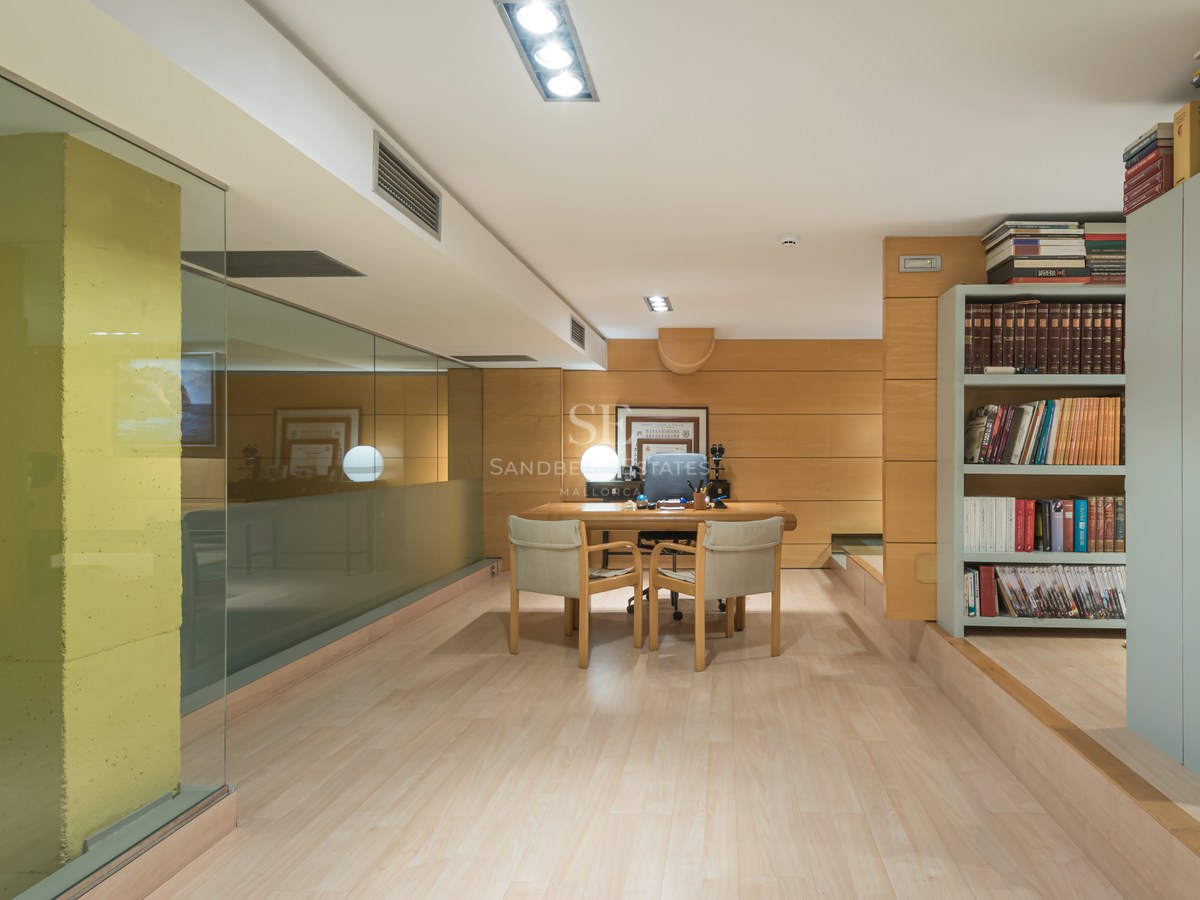 Modern home office featuring wood-paneled walls, a minimalist desk with two chairs, and floor-to-ceiling glass partitions.