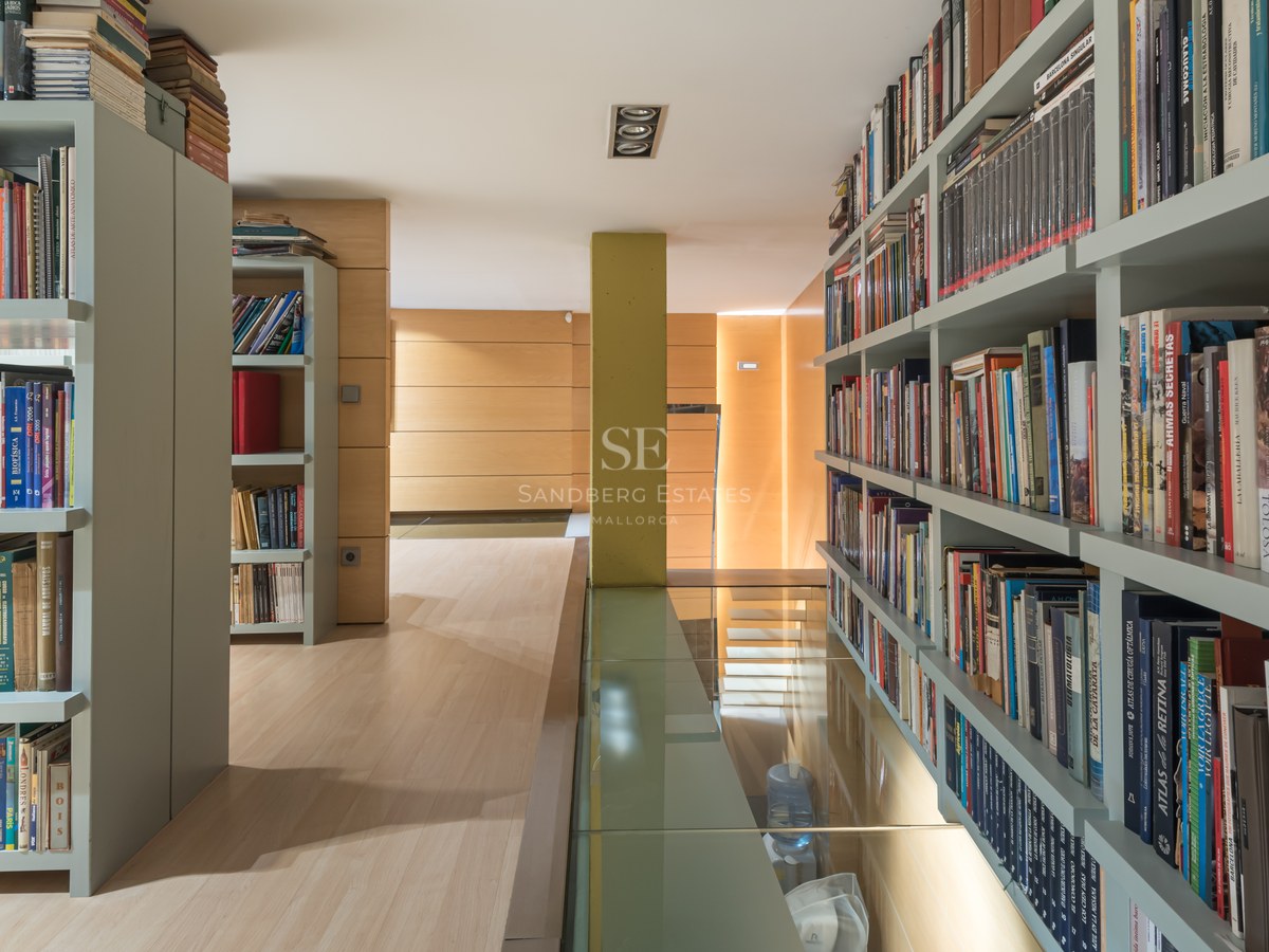 Modern home library with sage green floor-to-ceiling shelving, light wood floors, and a transparent glass floor panel.