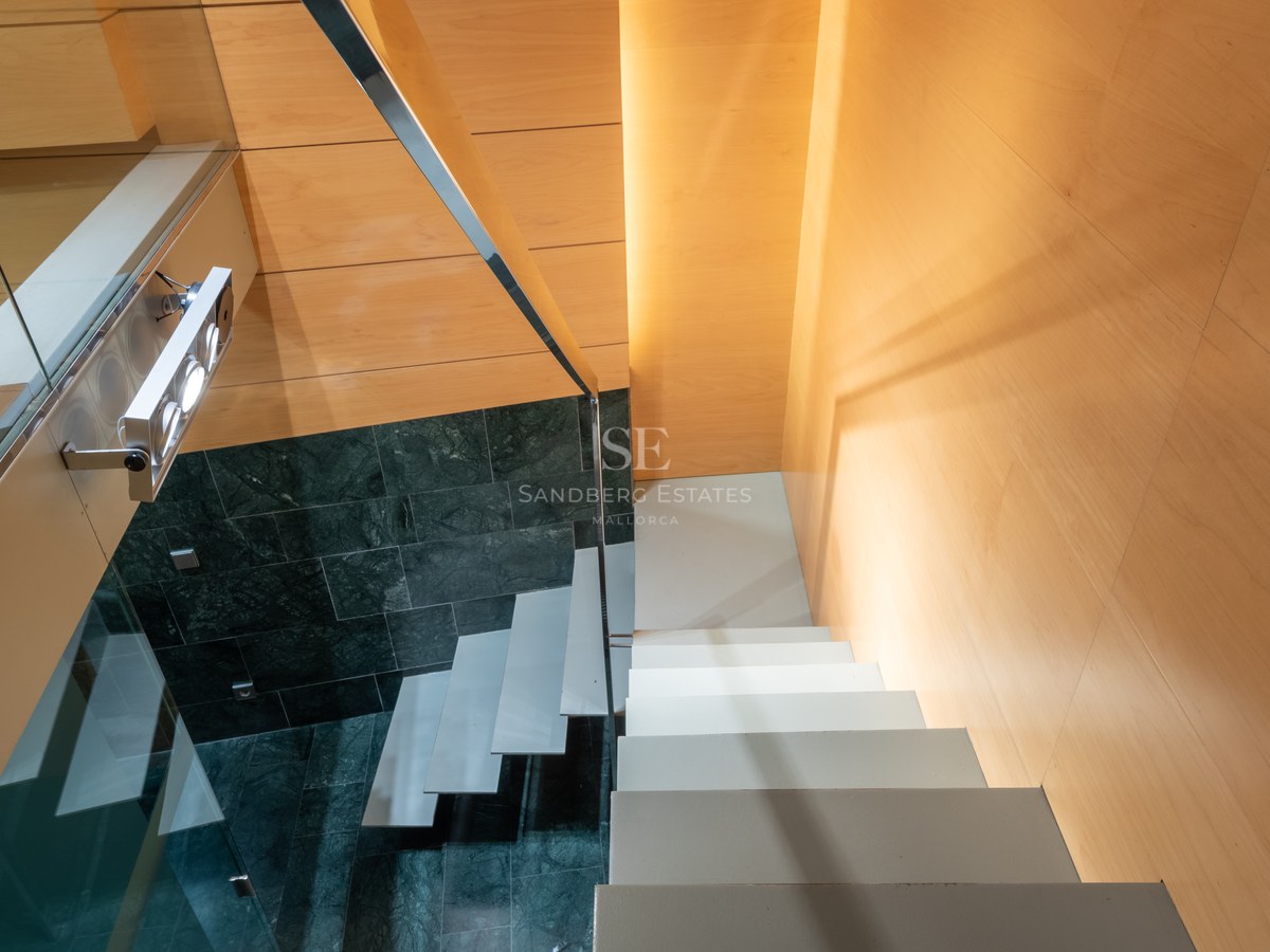 High-angle view of a modern staircase featuring white floating steps, dark green marble walls, and warm wood paneling.