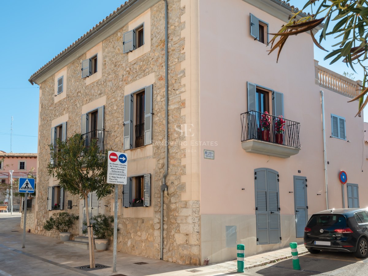 Bâtiment d'angle de trois étages avec façade en pierre naturelle, volets majorquins gris et balcons en fer forgé.