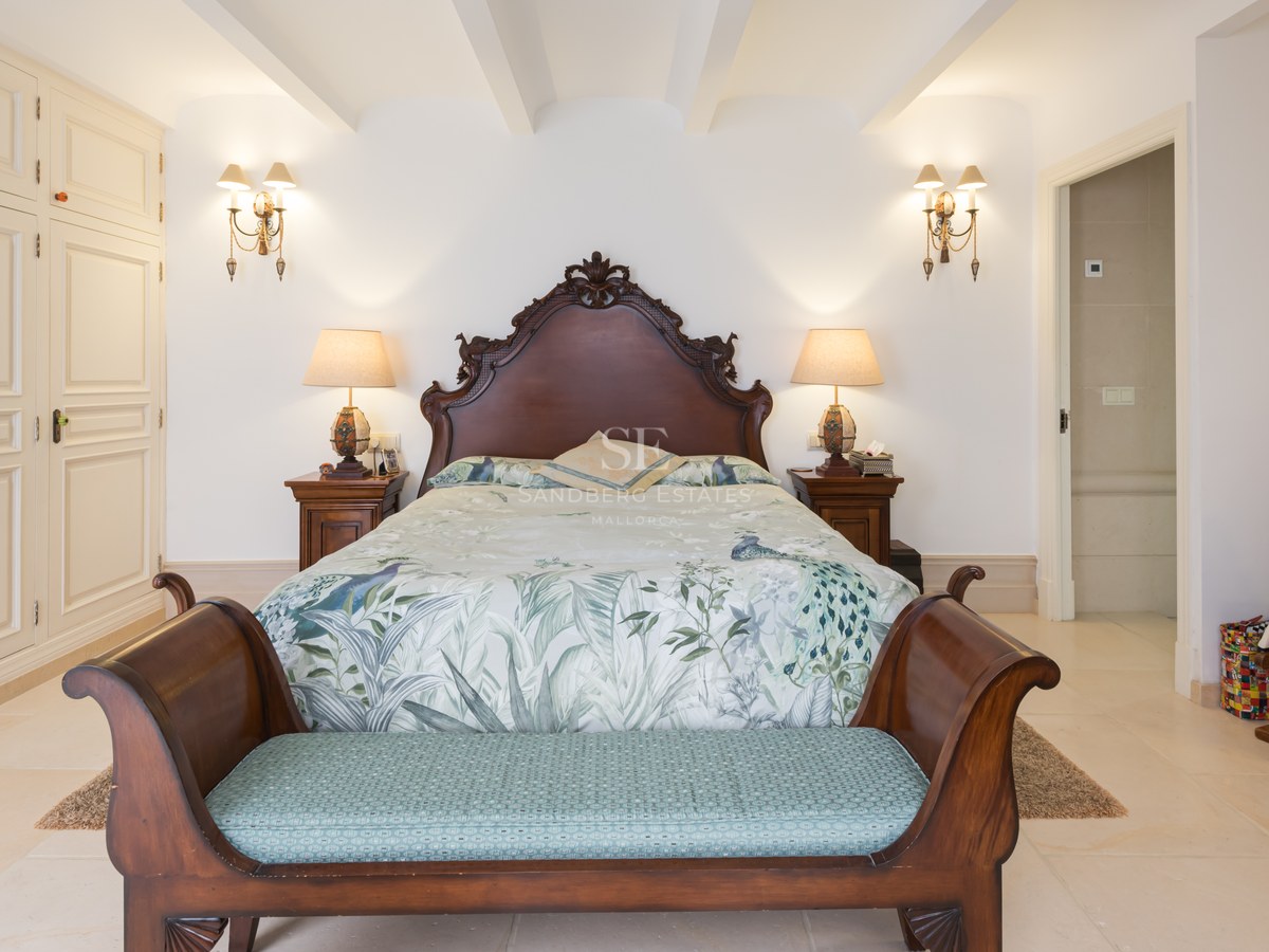 Chambre avec lit en bois sculpté, literie florale, banc au pied du lit et armoires encastrées blanches.