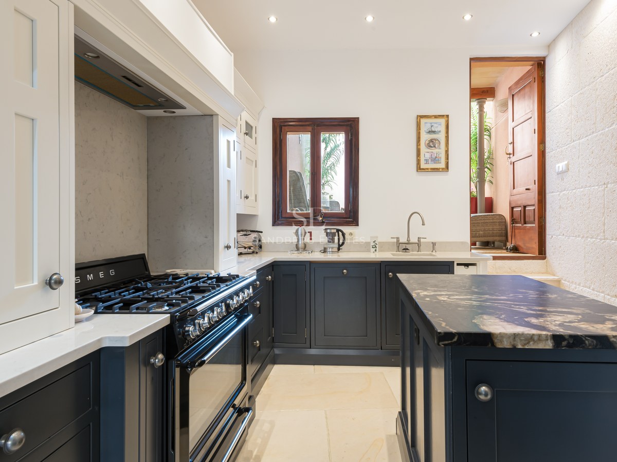 Cuisine avec des meubles bleu marine, des plans de travail en marbre blanc, une cuisinière Smeg et un mur en pierre.
