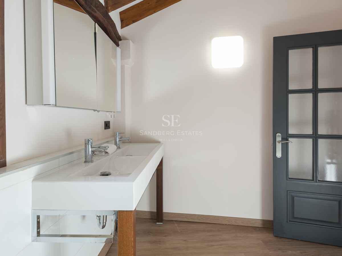 Salle de bain avec double lavabo blanc, poutres apparentes, porte gris foncé et armoire de toilette miroir.