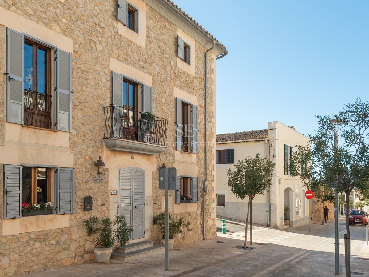 Immeuble en pierre traditionnelle avec volets gris et balcons en fer dans une rue ensoleillée.