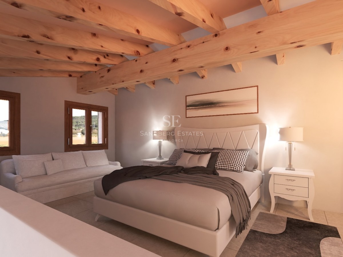 Bedroom with large bed, exposed wooden ceiling beams, white sofa, and windows looking out to the countryside.