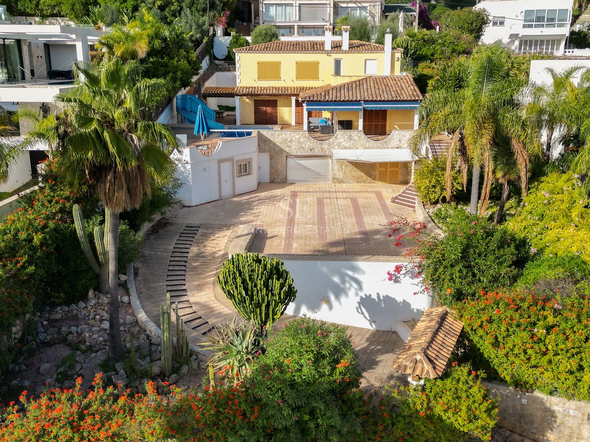 Luftaufnahme einer gelben mediterranen Villa mit Pool, Terrakottadach und üppiger tropischer Bepflanzung.